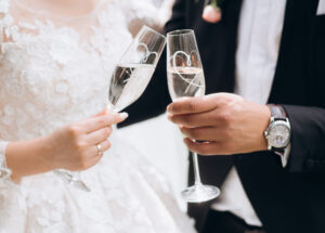 Groom with bride are knocking glasses with champagne