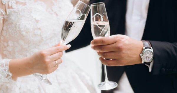 Groom with bride are knocking glasses with champagne