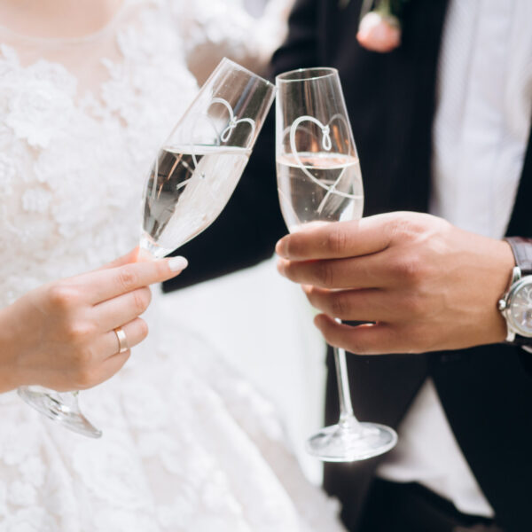 Groom with bride are knocking glasses with champagne